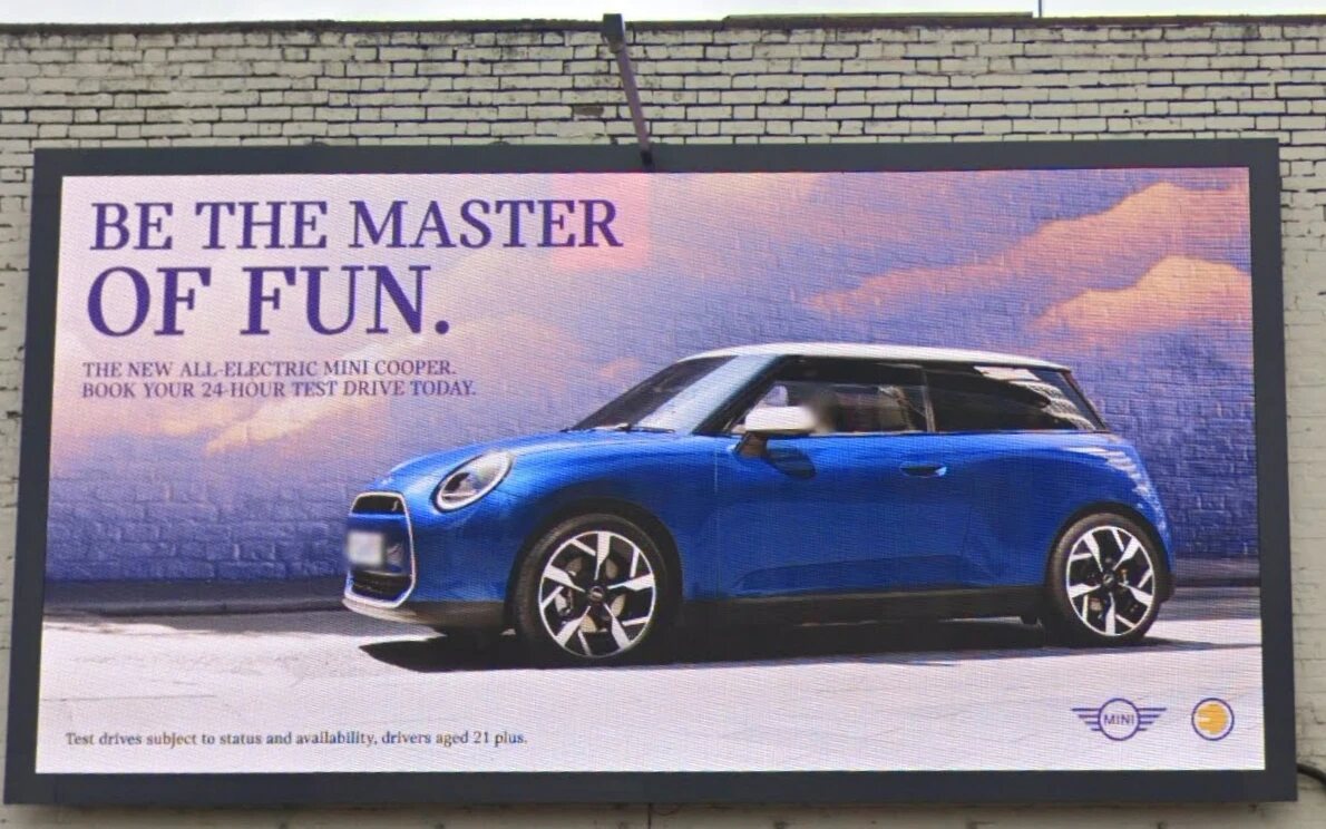 A digital advertising billboard mounted on a painted brick wall, showing a car advertisement
